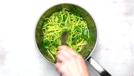 spaghetti and pesto being tossed in a pan