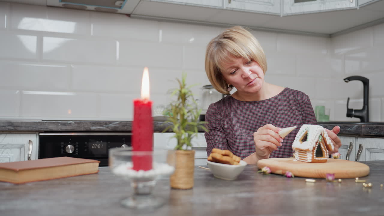 женщина тщательно глазурирует имбирный печенье, очищая избыток глазури с руки, праздничная атмосфера с красной свечой, горшки и миской печенья
