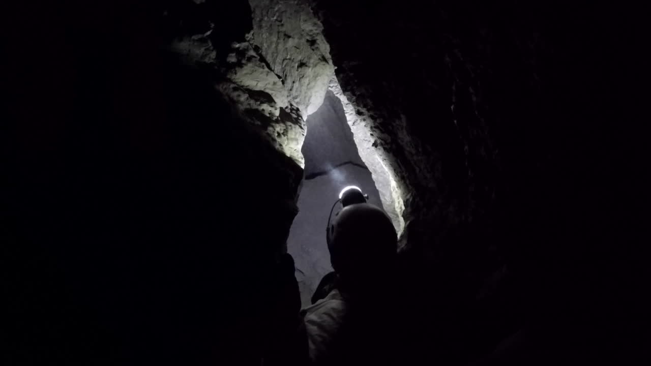 Female cave spelunker squeezes through snug dark passage in cave
