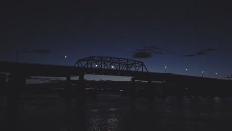timelapse of a semi-truck crossing a bridge at dusk under dramatic clouds. reflections ripple below on a calm river
