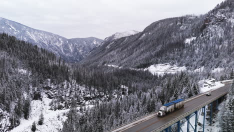 Semirremolques-Cruzando-Montañas-Vigilan-El-Puente-Paulson-En-La-Majestuosidad-Del-Invierno