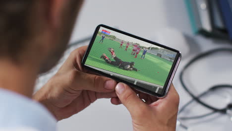compuesto de un médico masculino viendo un partido de hockey en un teléfono inteligente