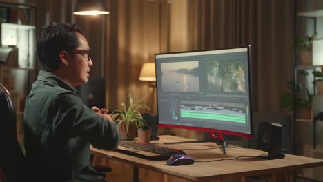 asian male video editor stretching while works with footage and sound on his personal computer, he works late at night