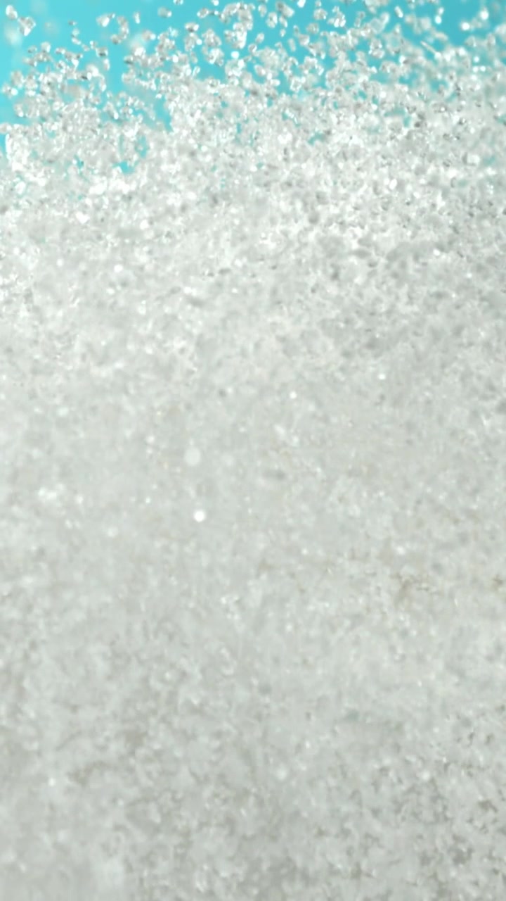 Cristalli di zucchero bianco che si disperdono su un vivace sfondo blu