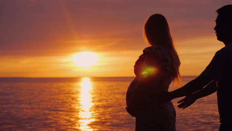 hombre asiático abraza a su esposa embarazada en un fondo de puesta de sol sobre el mar