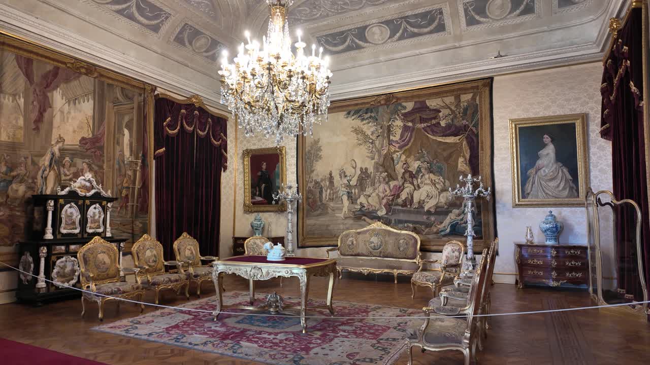Luxurious sitting room at the Palace of Ajuda in Lisbon, Portugal, showcasing antique furniture, crystal chandelier, and tapestry