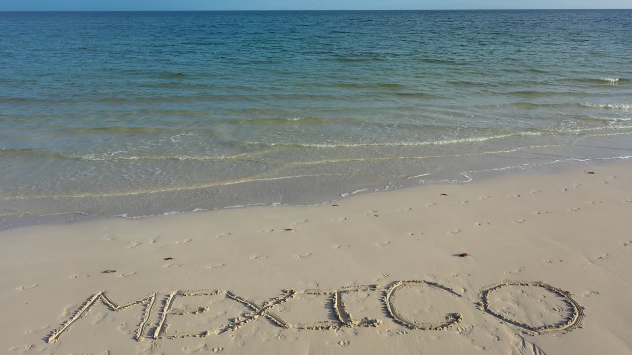 мексика, вписанная в песок на пляже, на горизонте видна голубая и изумрудная вода