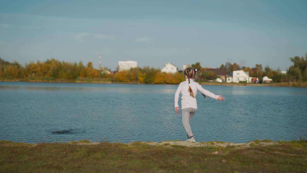 niña preescolar con trenzas largas lanza guijarros al río