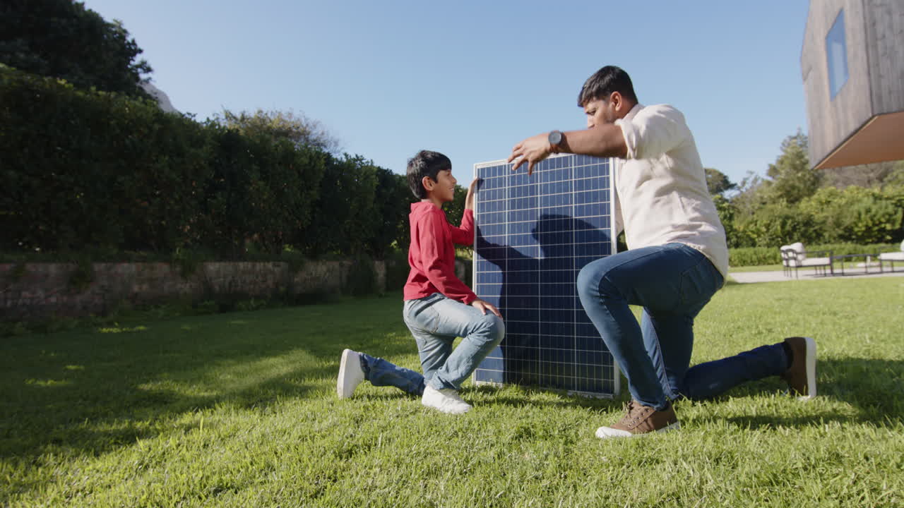 Indian father and son installing solar panel together in backyard on sunny day