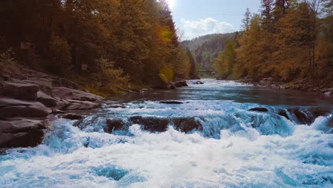 close up a low rapid flight over the rushing mountain river, blue in the middle of the forest and mountains. sunset time. the sun's rays give orange flare. the concept of freedom of decision-making, fresh natural food, fishing. dolly shot