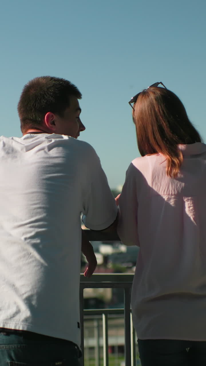 철의 레일링에 기대어있는 형제 자매들은 머리에 안경을 쓴 소녀와 따뜻하게 상호 작용합니다. 배경은 은 하늘 아래의 활기찬 도시 풍경을 보여줍니다.