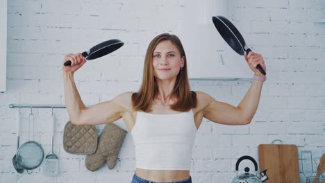 mooie vrouw met braaipannen thuis. muskulosere jonge vrouw met twee lege braaipanden. gezonde huisvrouw die voor de camera poseert.