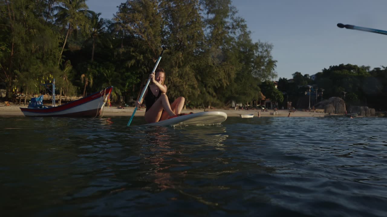 Woman enjoying paddleboarding on a tropical beach at sunset