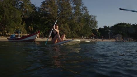 woman enjoying paddleboarding on a tropical beach at sunset