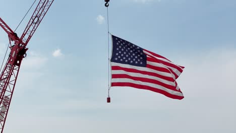 hung from a construction crane, the flag of the united states waves in the wind