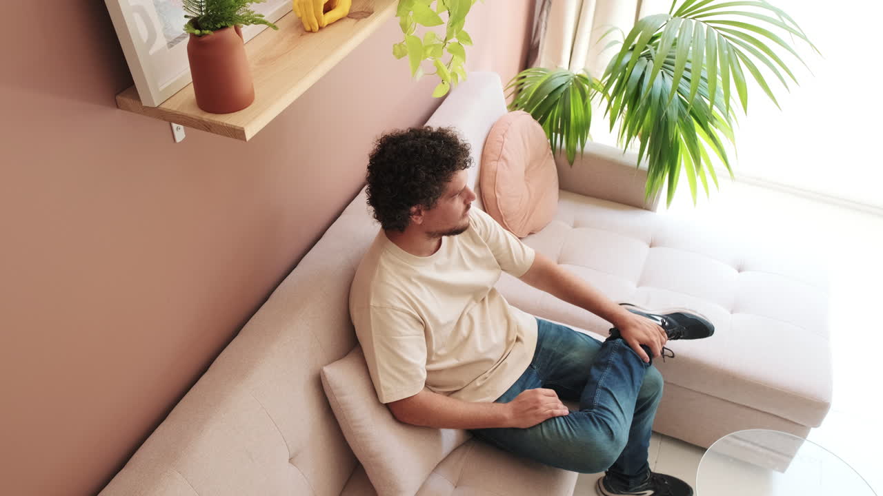 Young Man with Curly Hair Relaxing on Sofa in Modern Living Room