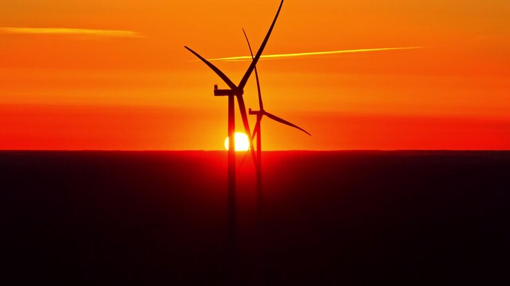 Zwei Windkraftanlagen als Silhouette vor einem glühenden orangefarbenen Sonnenuntergang, die Infrastruktur für erneuerbare Energien und dramatisches Abendlicht am Horizont einfangend