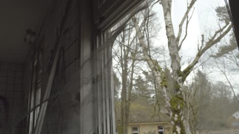 old window curtains in destructed window frame move in the breeze in lost place with view towards green forest during cold autumn, slow motion