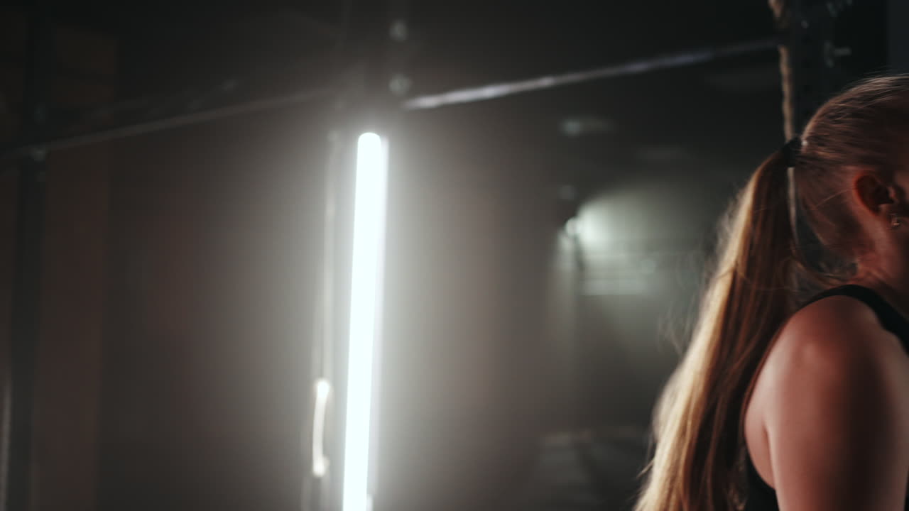 mujer joven descansando después de su entrenamiento y mirando hacia abajo. atleta femenina descansando después de un entrenamiento de fitness en un gimnasio oscuro