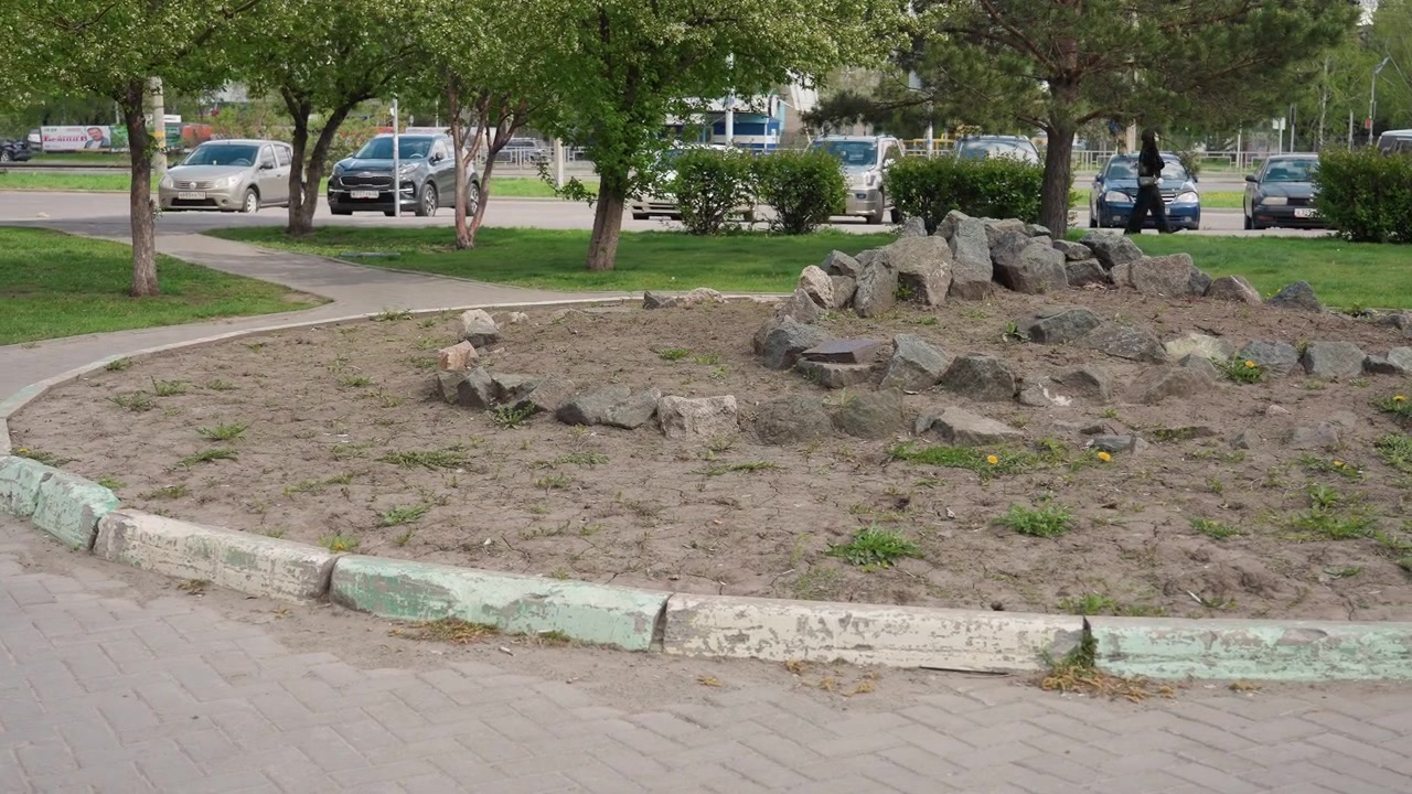 Dagutsikt over en bypark med et steinete blomsterbed og trafikk