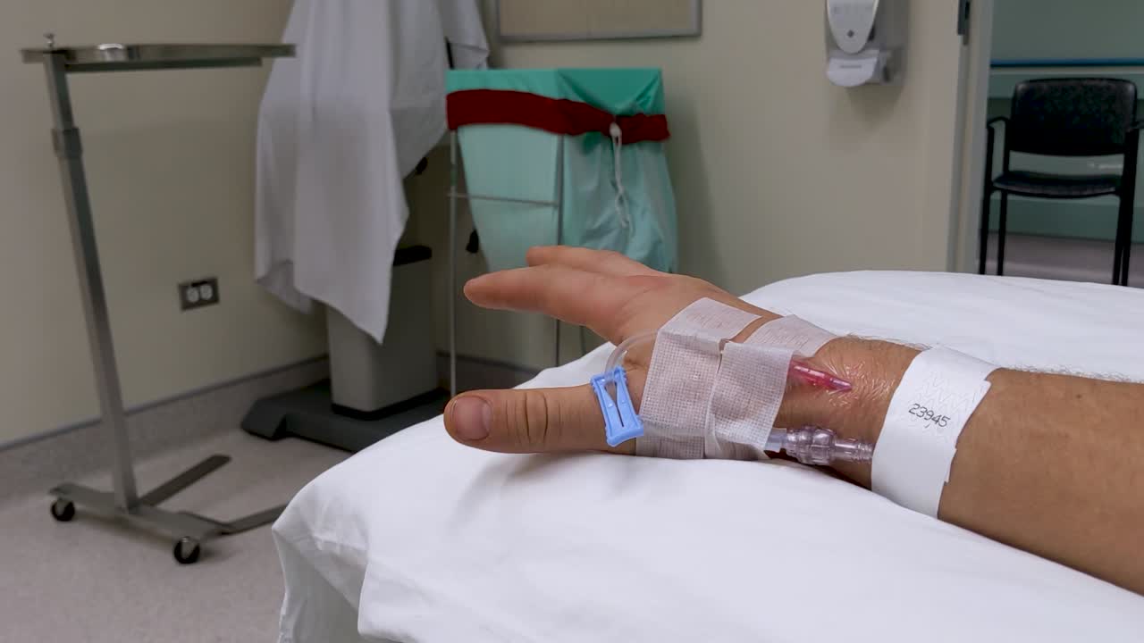 movimientos lentos de la mano de la mano derecha masculina caucásica irreconocible en un escenario médico con iv en la muñeca