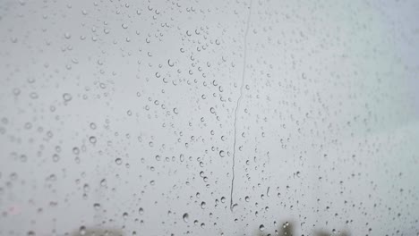 a slow-motion footage of a close-shot of heavy rain drops is seen through a window glass