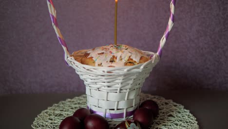 pastel de pascua festivo con una vela en una canasta de mimbre y unos cuantos huevos de colores debajo