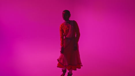 Full-Length-Studio-Shot-Of-Female-Kathak-Dancer-Performing-Dance-Wearing-Traditional-Indian-Dress-Against-Purple-Background