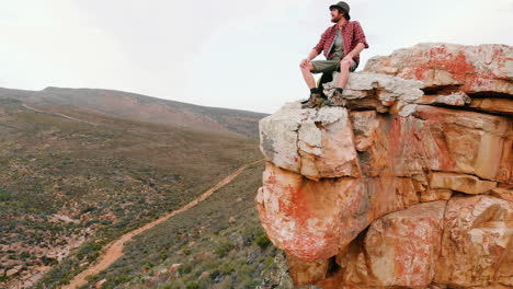 young caucasian man sits atop a rugged cliff, gazing into the distance with copy space