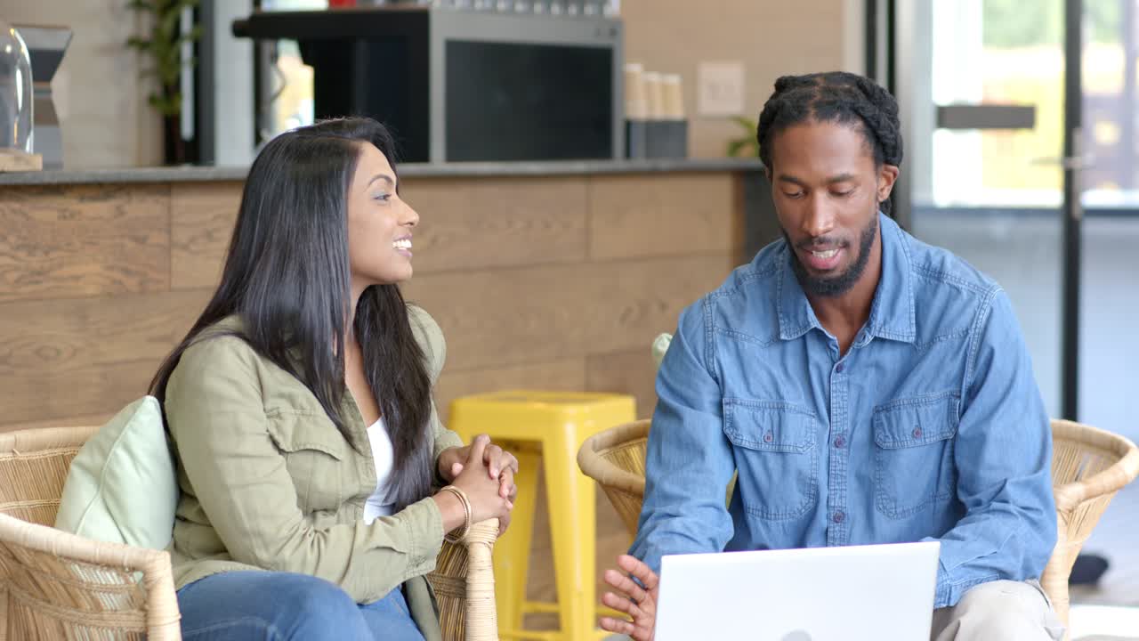 African American man and Indian woman gesturing and scrolling on laptop in lounge reviewing content