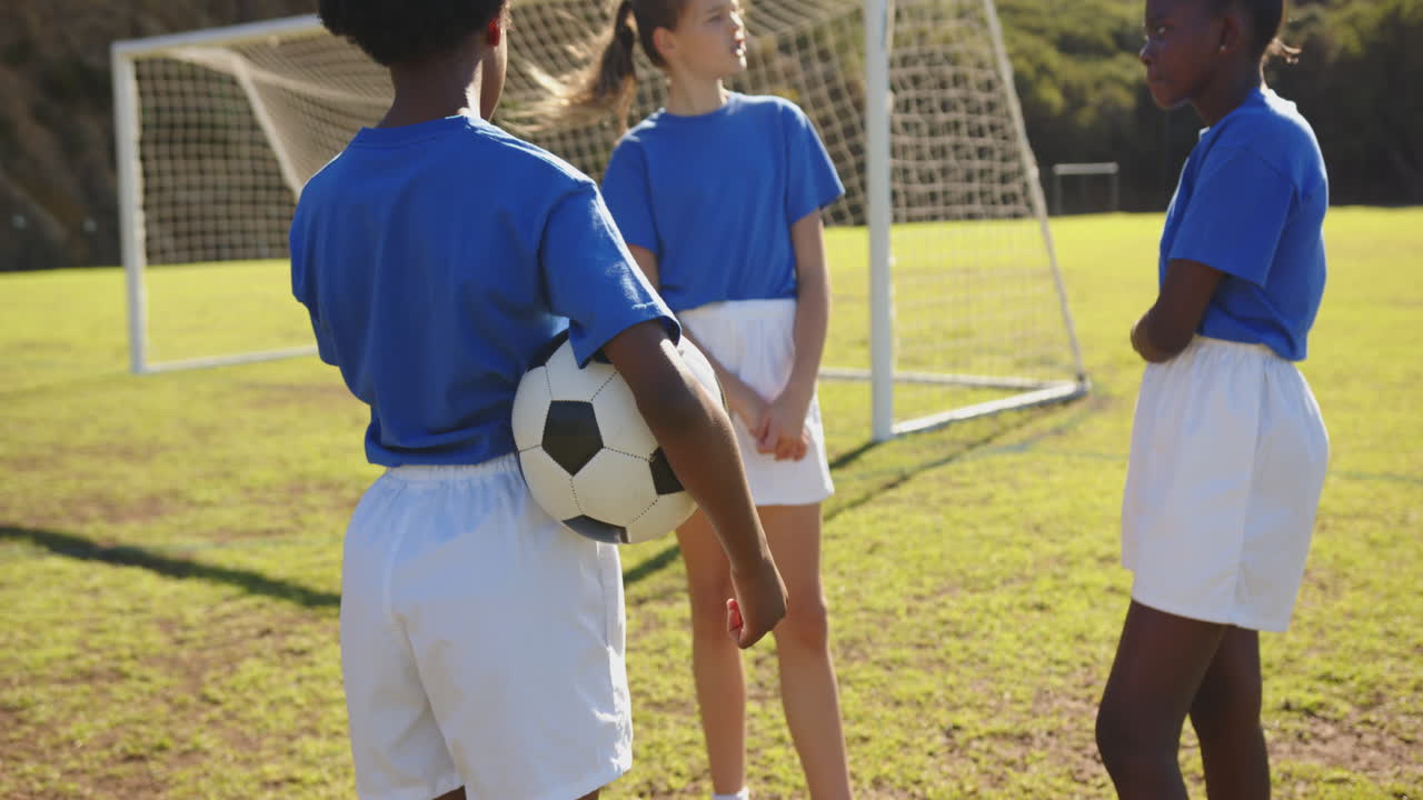 Playing soccer, girls in school uniforms standing on field near goalpost