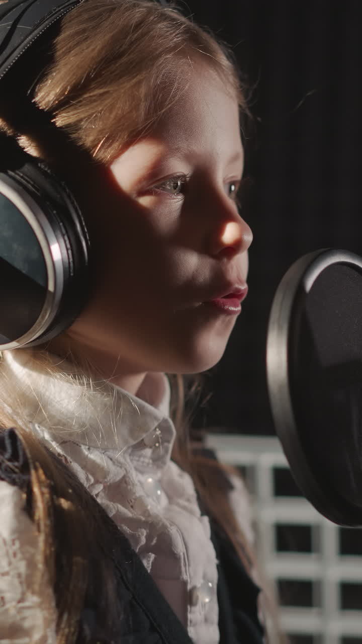 niño canta una canción en un estudio de grabación de audio. una niña linda con auriculares canta en un micrófono con filtro en una habitación aislada de sonido. niño talentoso