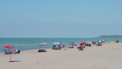 la gente toma el sol mientras se sienta en la playa a orillas del mar mediterráneo en alicante, españa