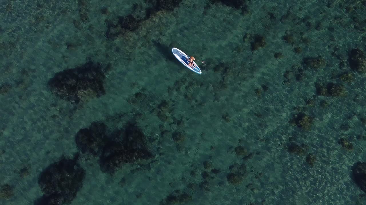 Veduta a volo d'uccello di una persona che fa paddleboard in acque tropicali limpide.