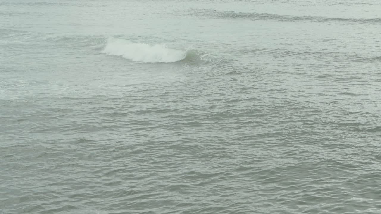 gentle waves move slowly across calm sea in muted cloudy light