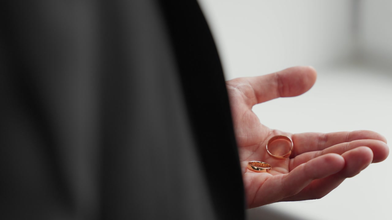 Detailed view of a hand holding gold rings, creating an intimate and thoughtful mood. Soft lighting enhances the focus on the jewelry, perfect for themes of love and commitment.