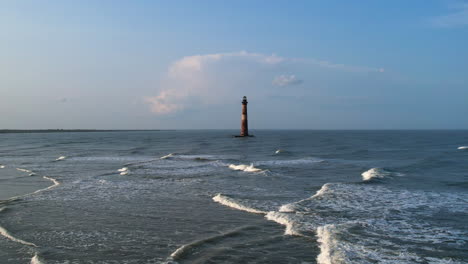 a drone shot moving towards a lighthouse that is surrounded by the ocean.