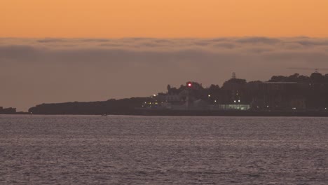 Schöner-Nachtuntergang-Mit-Großem-Orangefarbenem-Himmel-Und-Dunklen-Wolken-Mit-Leuchtturm,-Der-In-Cascais-Licht-Gibt