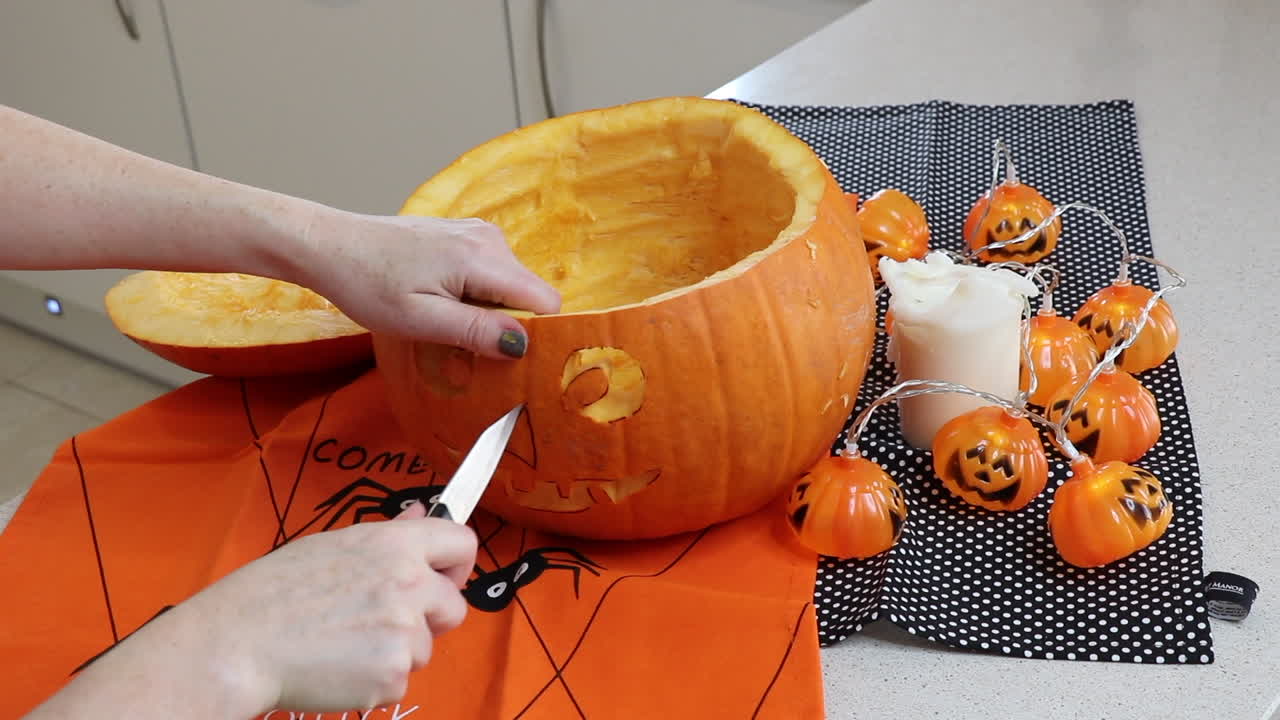 mujer tallando una cara aterradora en una calabaza naranja jack o'lantern en casa en la cocina