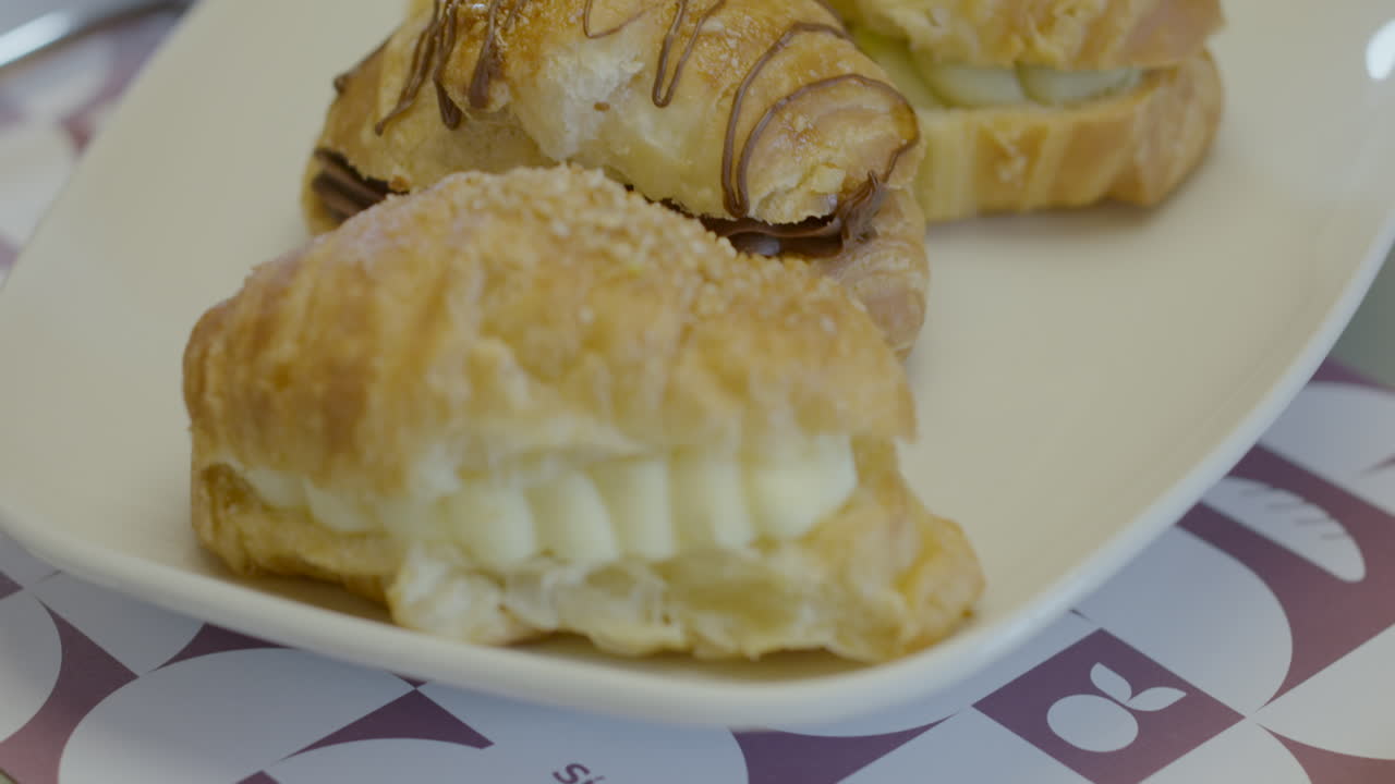 Close-up of three puff pastry croissants filled with cream, presented on a white plate. Golden, crispy and fresh texture