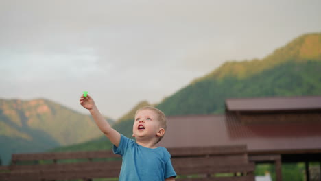 excited boy launches flying toy on ground against mountains