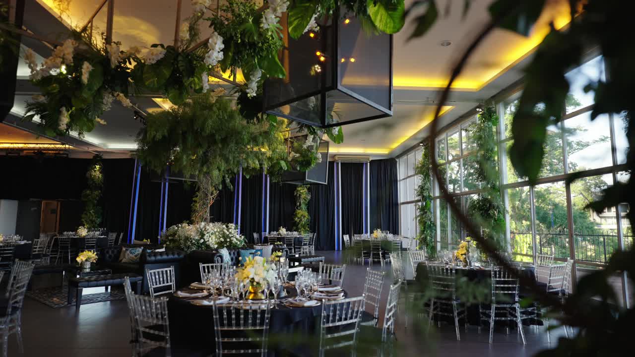 Cámara lenta que revela un elegante salón de bodas con iluminación ambiental, arreglos florales, mesas decoradas y un diseño sofisticado del espacio