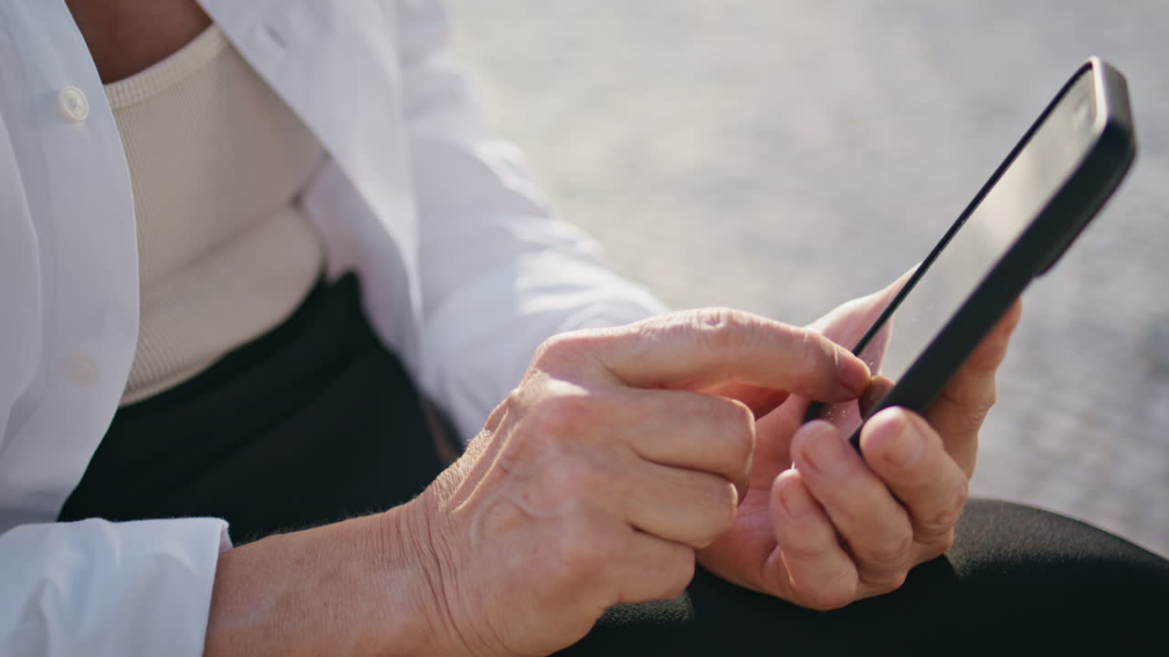 시니어 손이 드폰 화면을 만지고 거리에서 인터넷을 탐색하고 있습니다.