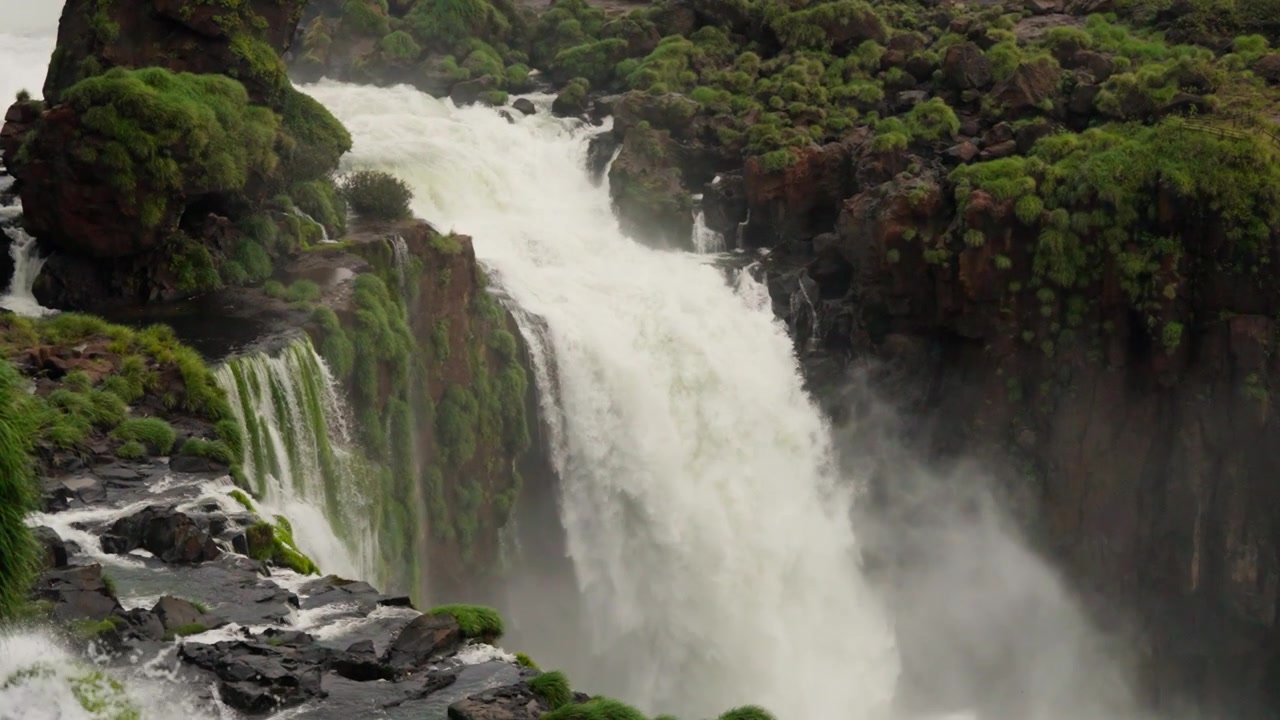 Cachoeira fluindo sobre pedras verdes musgosas cercada por plantas tropicais em câmera lenta