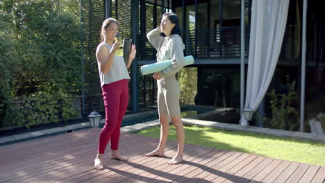 happy asian female friends with exercise mats and water bottle smiling on terrace, slow motion