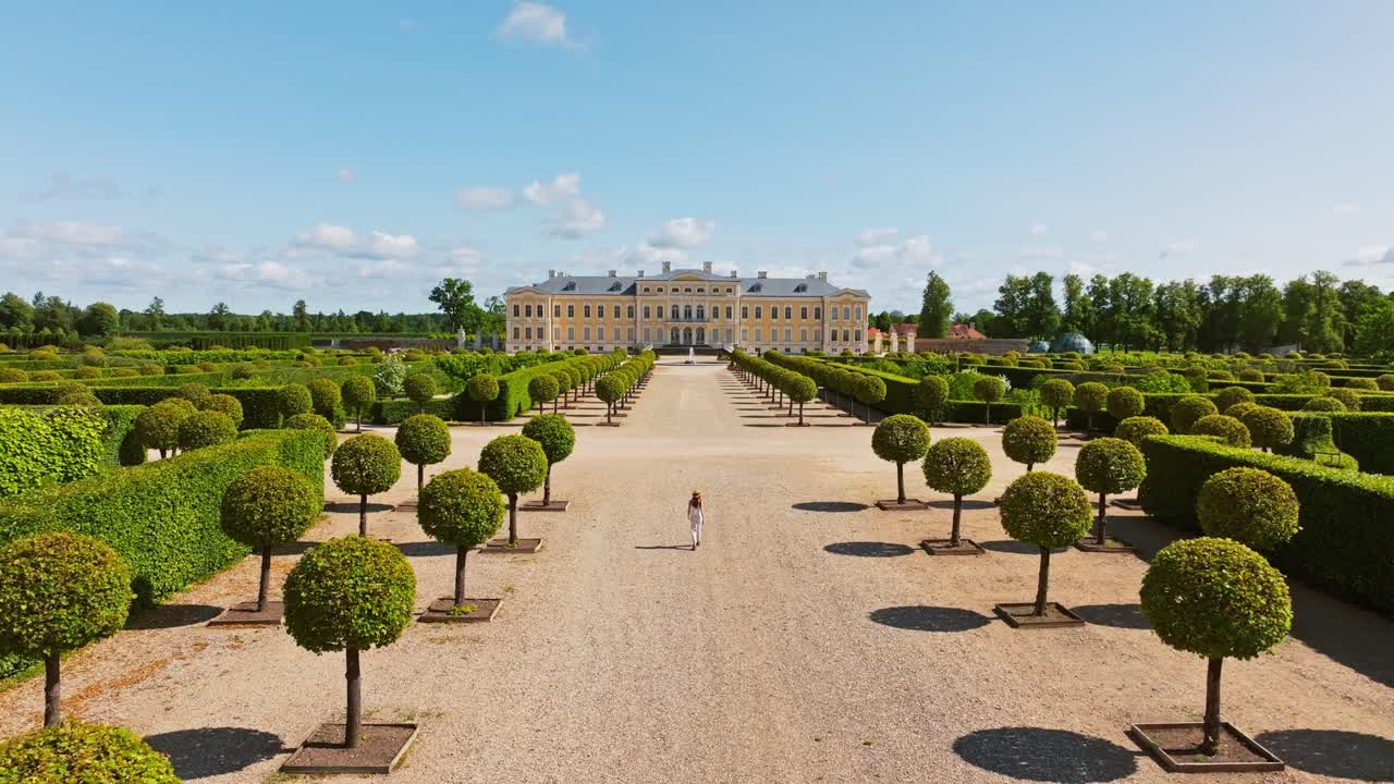 Ripresa aerea di donna in bianco che cammina nel giardino del palazzo con perfetta simmetria