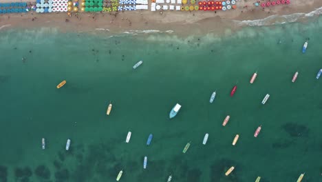 Vista-Aérea-De-Pájaro-De-Arriba-Hacia-Abajo-Del-Famoso-Puerto-De-Galinhas-O-Playa-De-Puerto-De-Pollo-En-Pernambuco,-Brasil-Con-Sombrillas-Coloridas,-Turistas-Nadando-En-Las-Piscinas-Naturales-Y-Veleros-Anclados