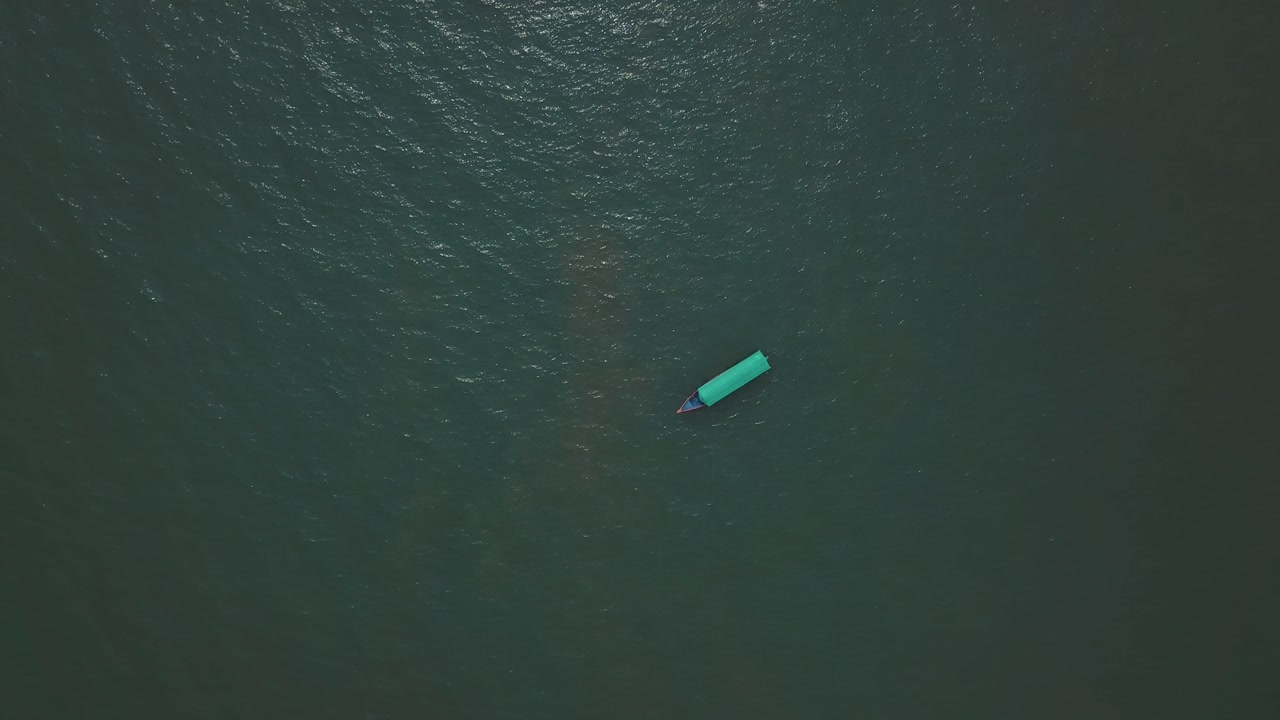 Aerial view of a single turquoise-colored boat floating on dark green ocean waters near Malvan, Maharashtra, India. The boat moves gently across the textured sea surface.