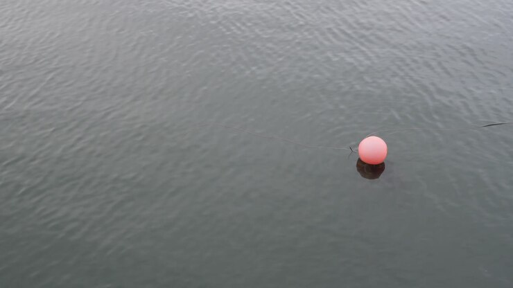 Faded solo red sea buoy floating on blue green water