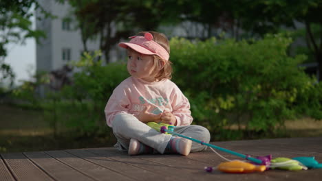 young girl sitting on deck taking break from playing with toy fishing set